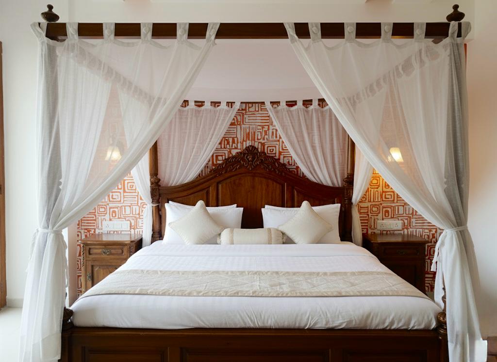 Master bedroom interior with four-poster canopy bed, sheer drapes and carved wooden headboard by Assankhhya