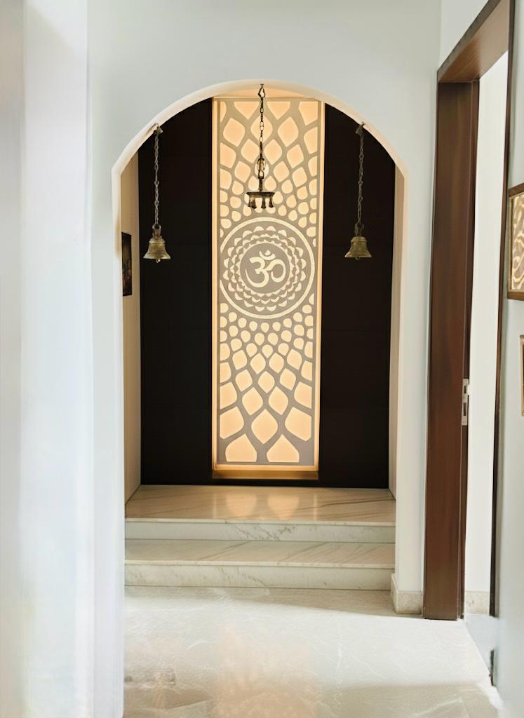Custom pooja room design with backlit Om panel, arched doorway and brass bells by Assankhhya